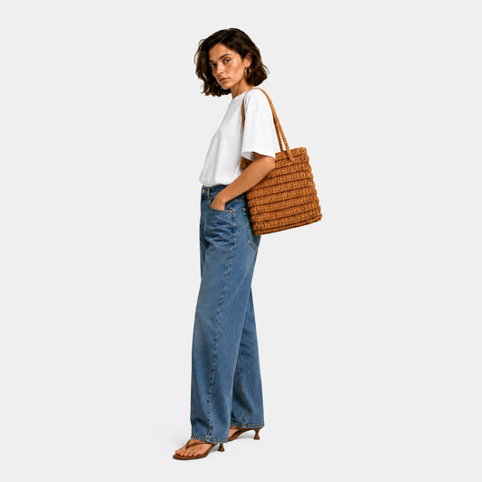Model carrying THE STAPLE BAG in tan over her shoulder, side view with white tee and wide-leg denim