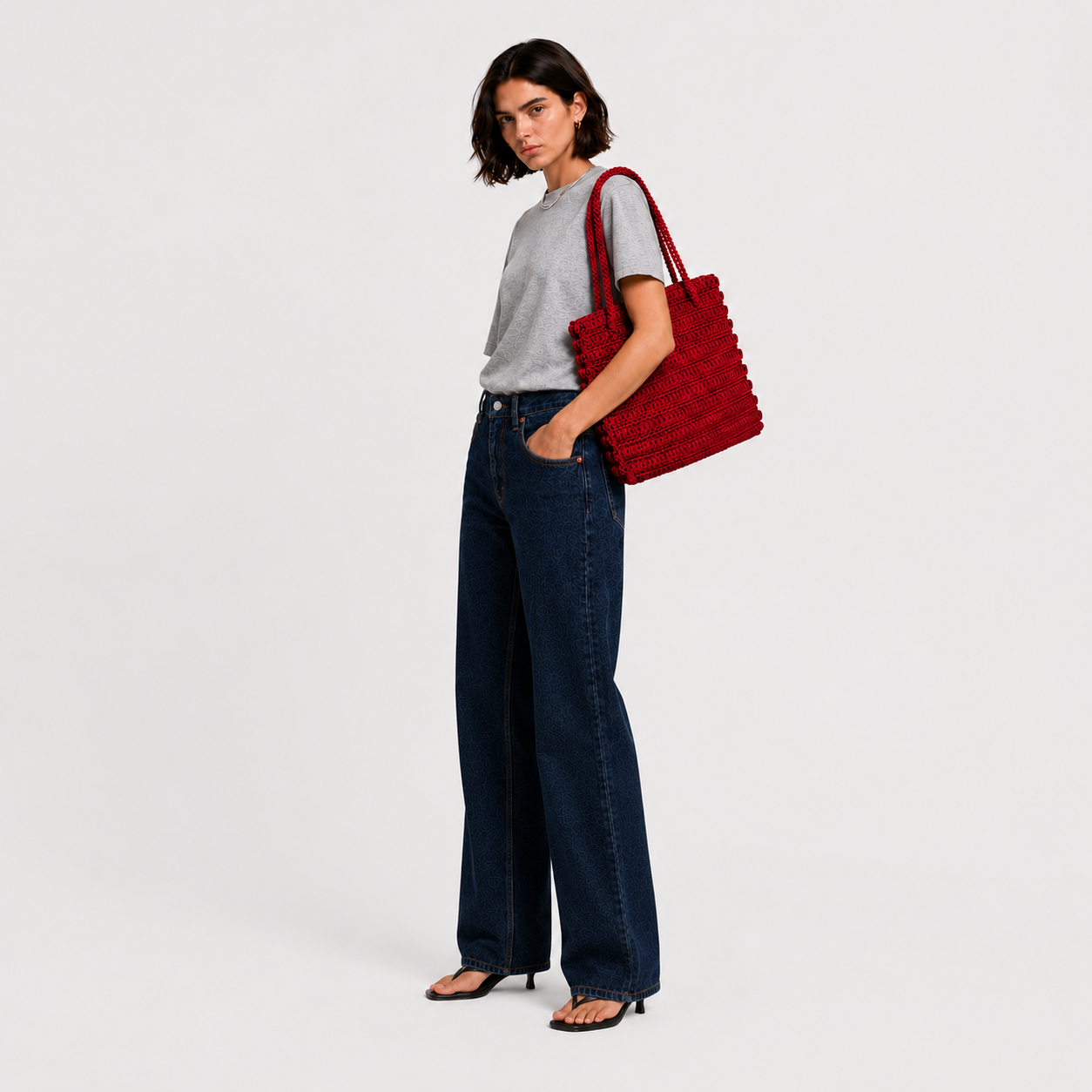 Model carrying THE STAPLE BAG in red over her shoulder, side view with grey tee and wide-leg denim