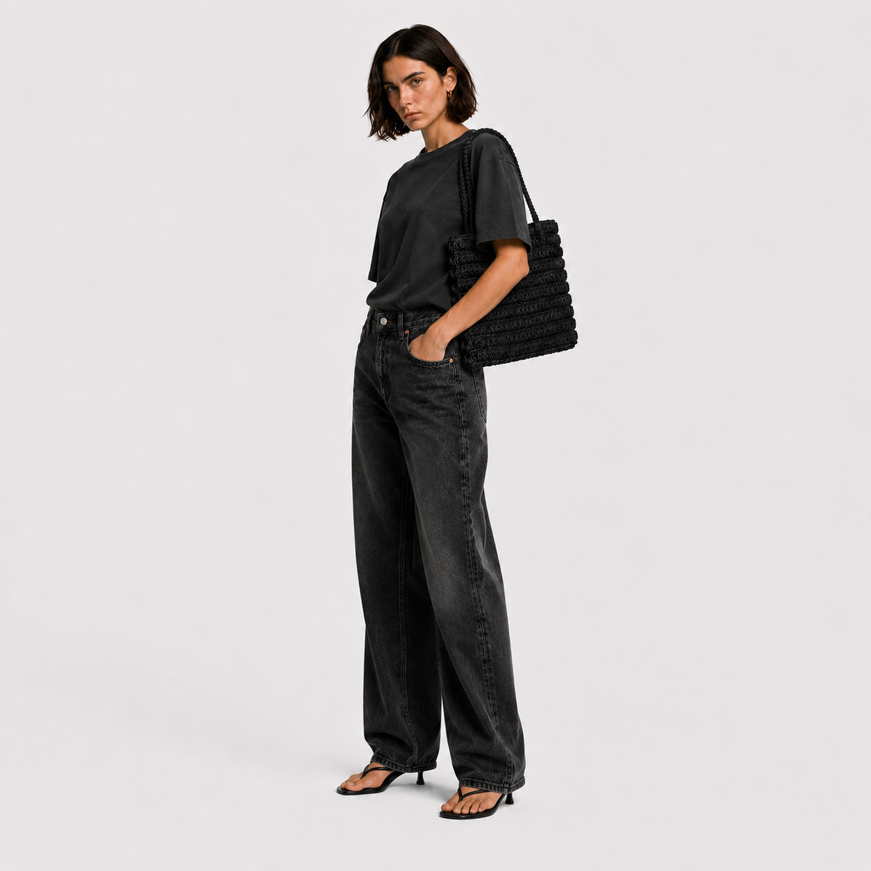 Model carrying THE STAPLE BAG in black over her shoulder, side view with black tee and dark denim