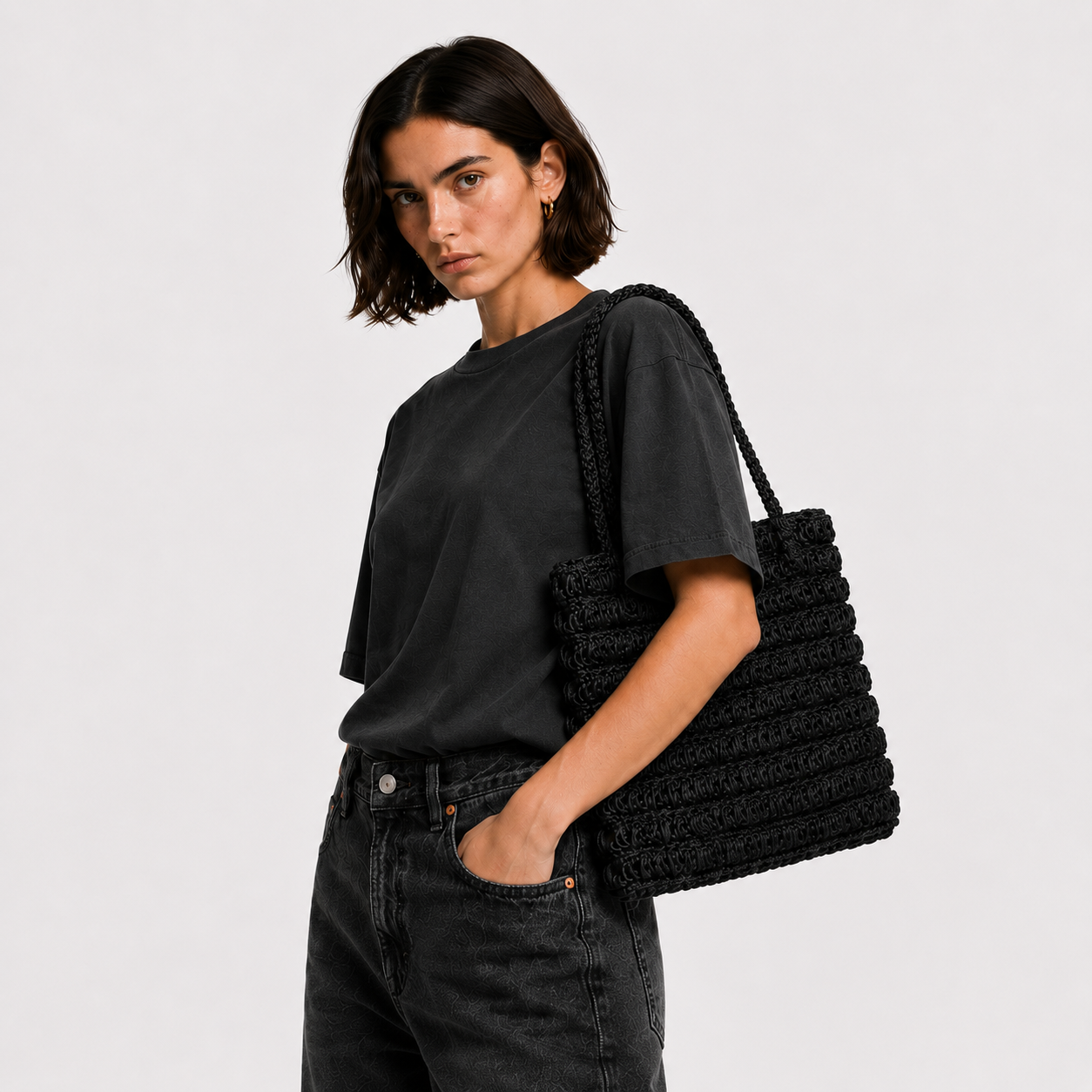 Close-up of THE STAPLE BAG in black on model's shoulder, hand-crocheted leather texture visible